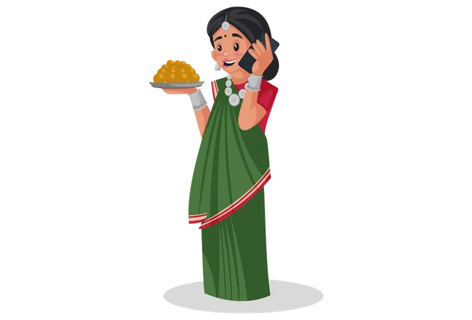 Gujarati woman is holding a sweets plate in hand and talking on mobile phone  Illustration