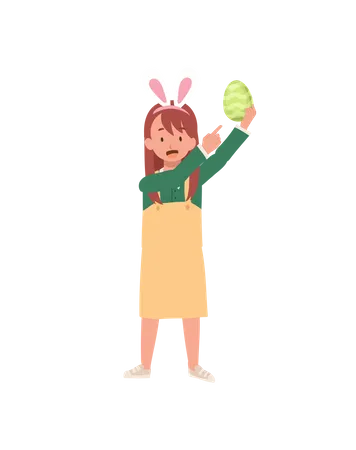 Menina feliz com orelhas de coelho segurando ovo de Páscoa enquanto aponta o dedo indicador para mostrar  Ilustração